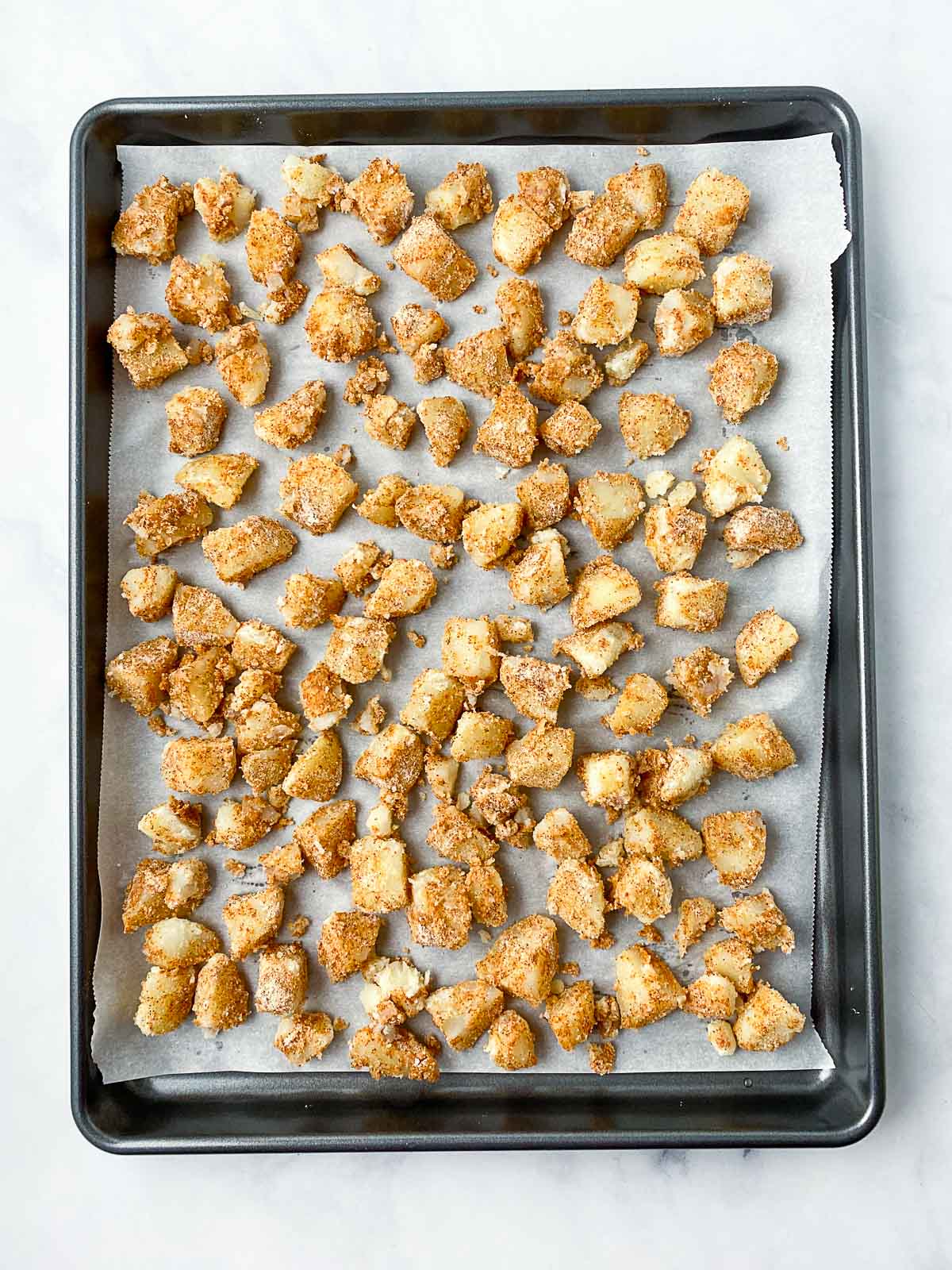 Seasoned diced potatoes on a parchment lined baking sheet.