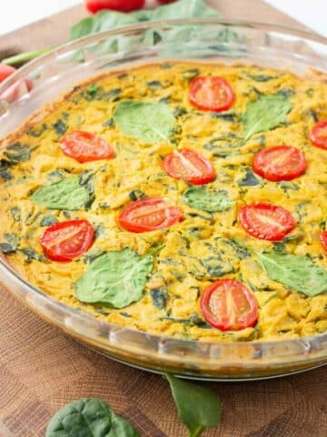 Tofu frittata in a glass pan sitting on a wooden cutting board/