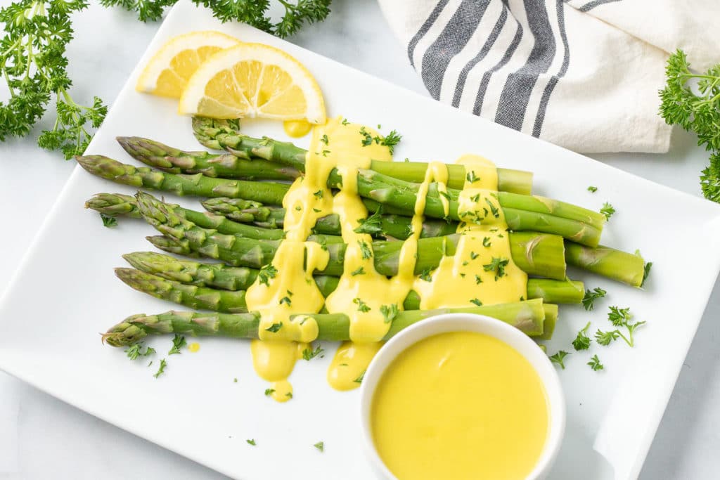 Overhead image of asparagus with hollandaise sauce and small dish of hollandaise.
