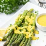 Asparagus with hollandaise sauce on a white platter.