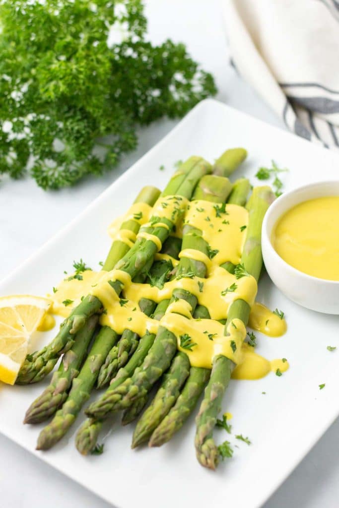 Asparagus with hollandaise sauce on a white platter.