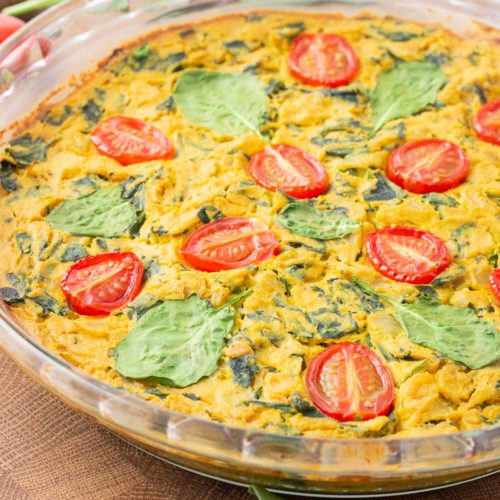 Tofu frittata in a glass pan sitting on a wooden cutting board/