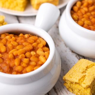 Two bowls of baked beans with surrounded by pieces of cornbread.