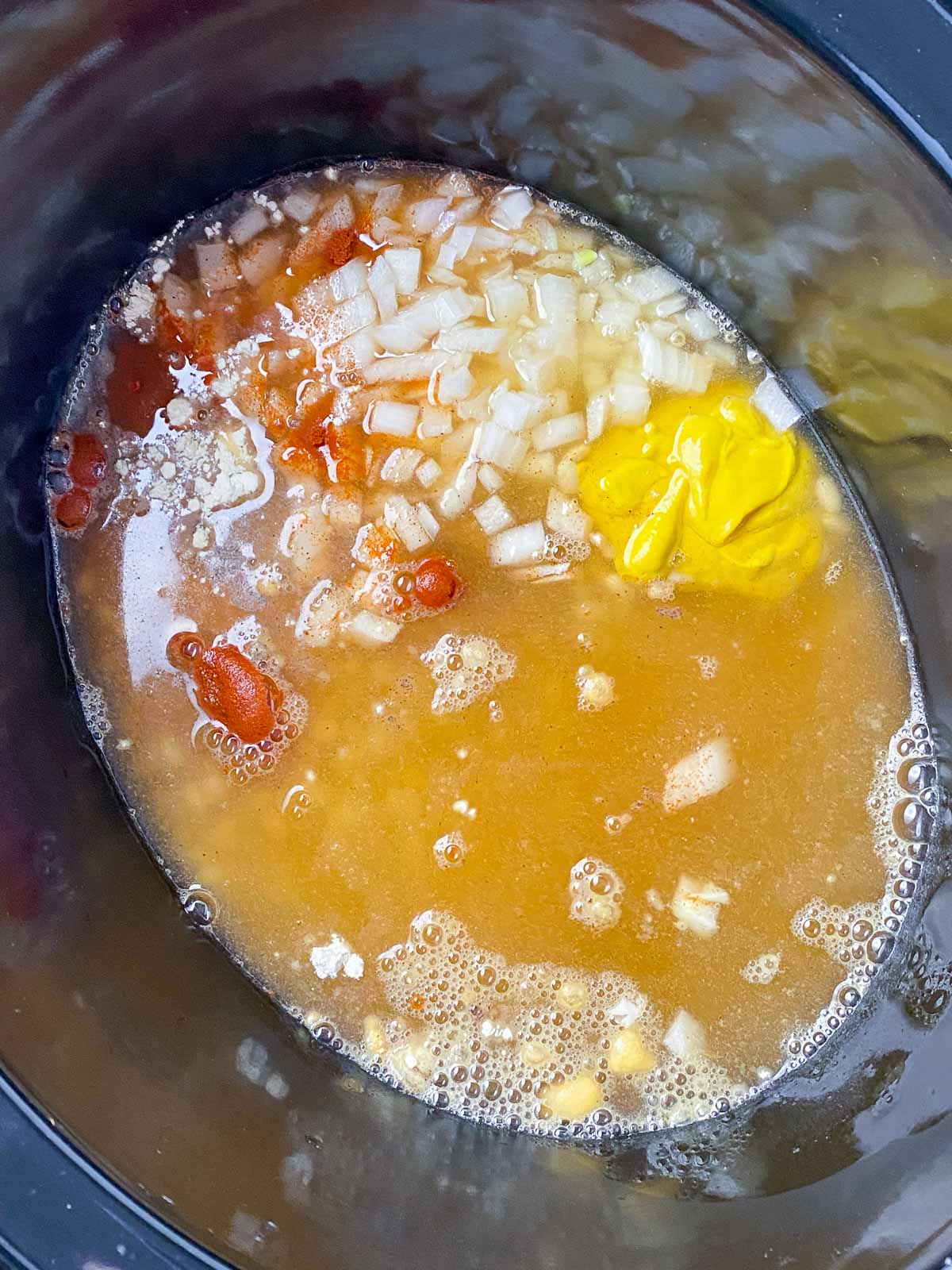 Vegetable broth added to baked beans ingredients in crockpot.