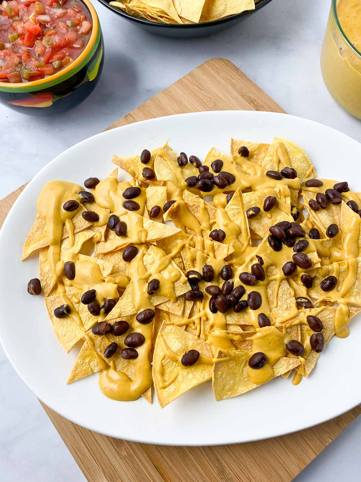 First layer of tortilla chips, cheese sauce, and black beans on nacho platter.