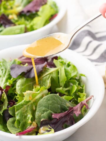 Honey mustard dressing being drizzled from spoon onto bowl of salad.