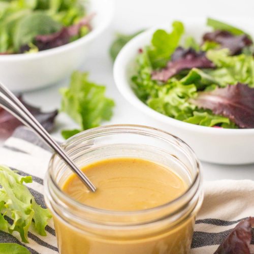 Jar of honey mustard dressing with bowls of salad in background.