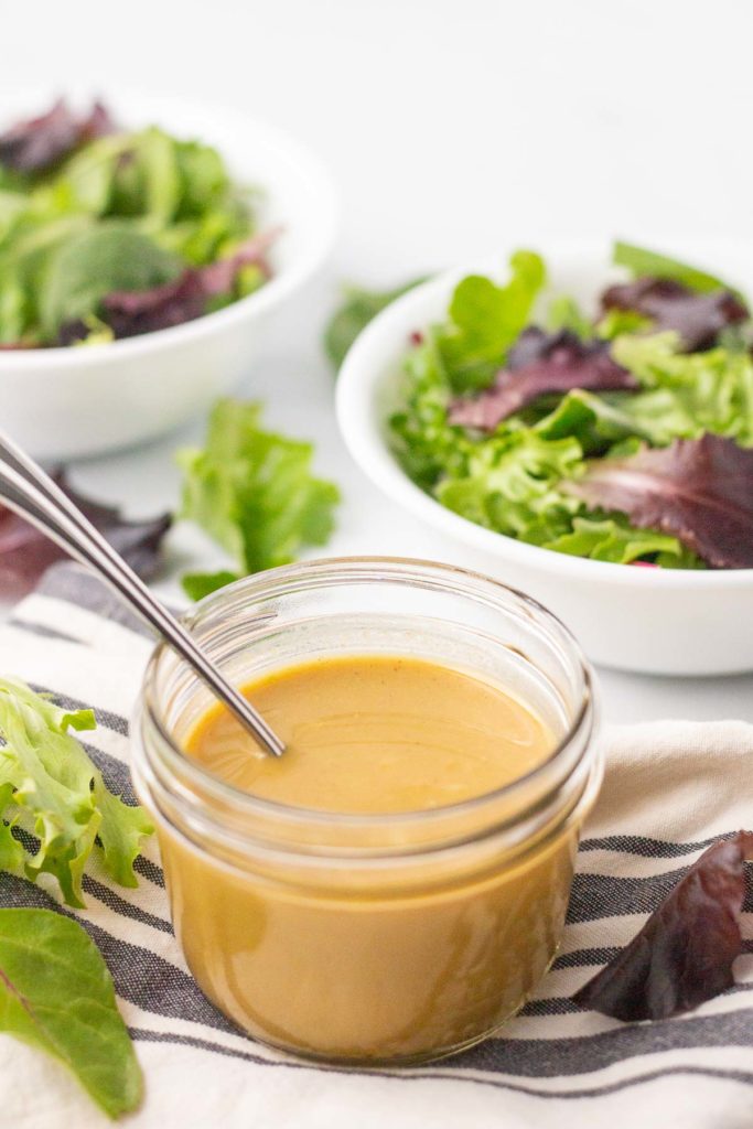 Jar of honey mustard dressing with bowls of salad in background.