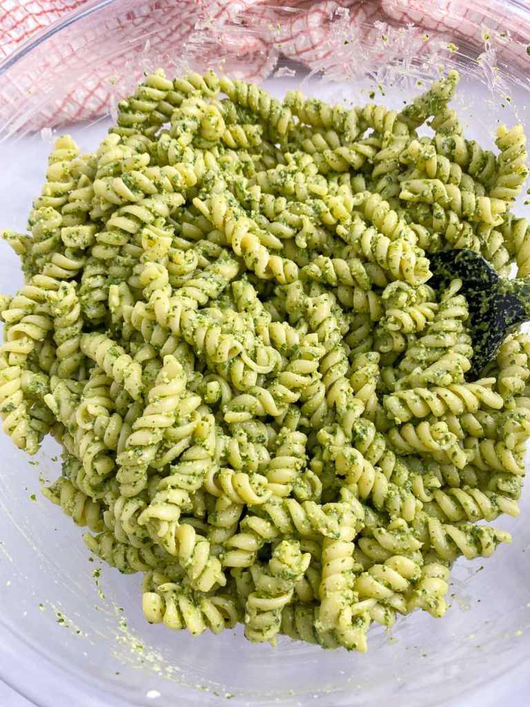 Pesto mixed into pasta in large mixing bowl.