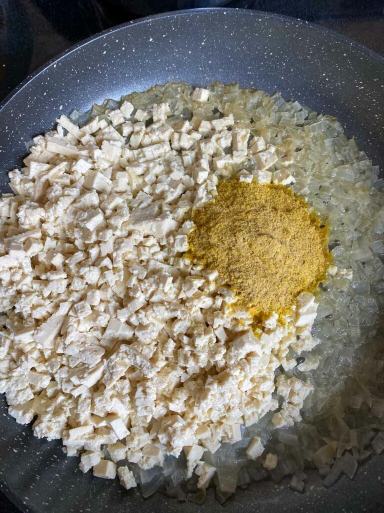 Tofu and seasonings added to pan of sauteed diced onions.