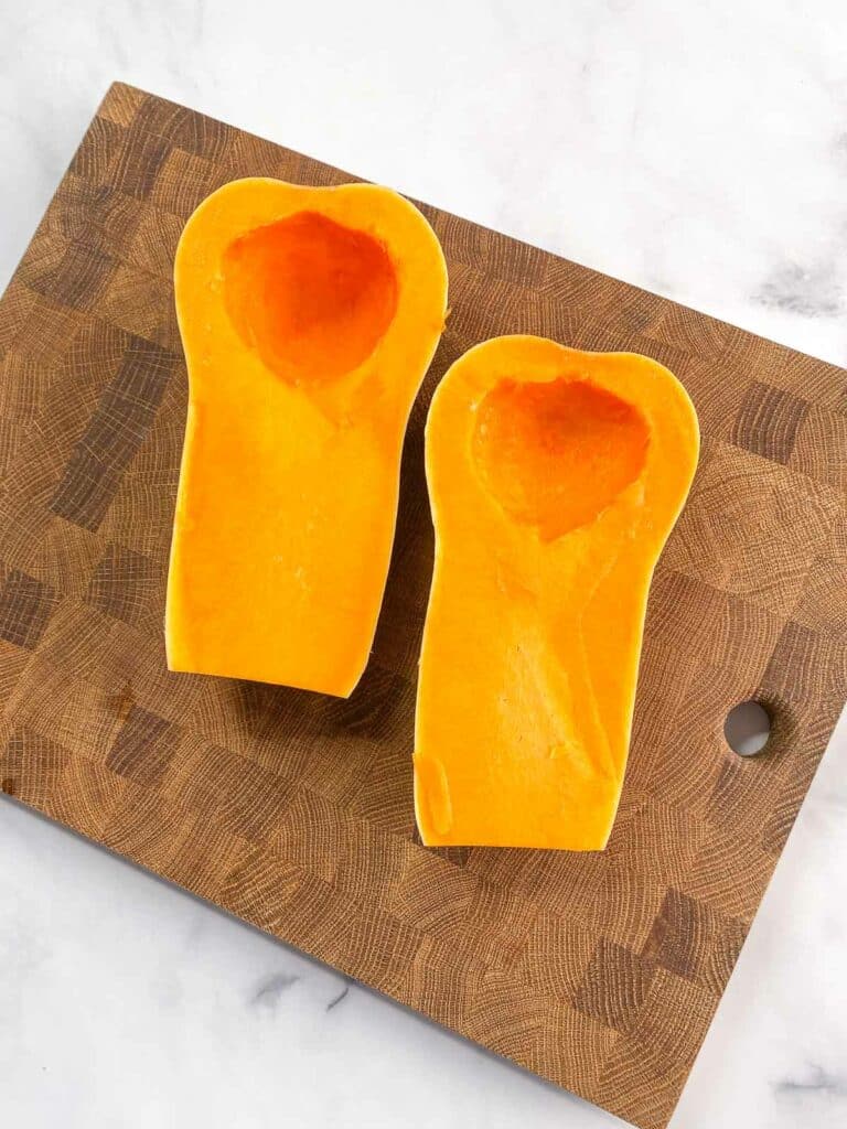 Halved and seeded butternut squash on a wooden cutting board.