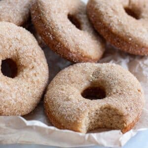Cinnamon sugar donuts on parchment paper with a bit taken out of one of them.