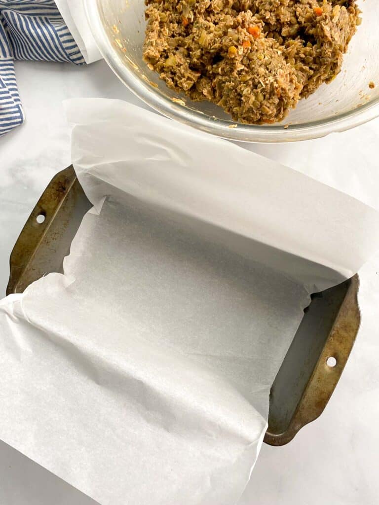 Loaf pan lined with parchment paper in front of a bowl of lentil loaf mixture.