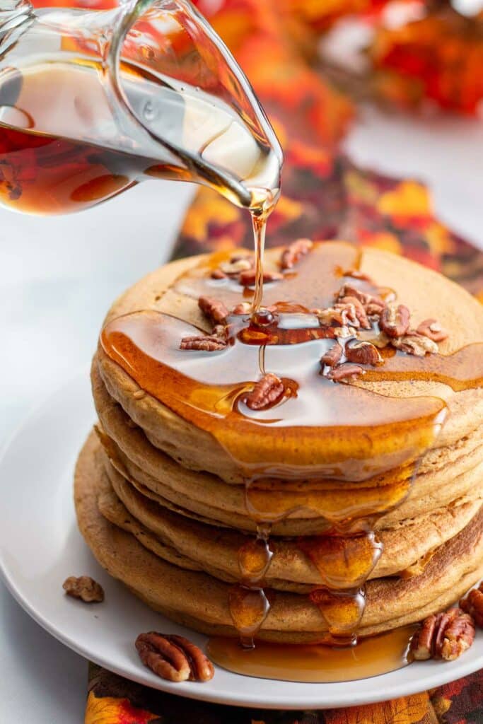 Maple syrup being poured over stack of vegan pumpkin pancakes.