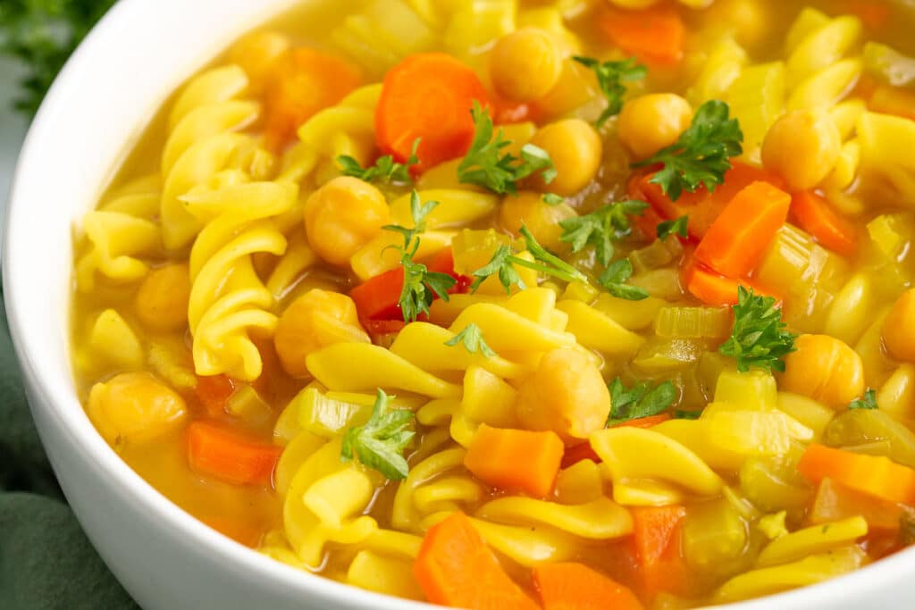 Closeup image of chickpea noodle soup in a white bowl.