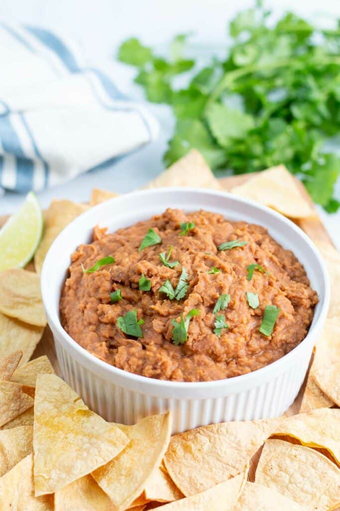 Bowl of refried beans garnished with chopped cilantro, surrouded by tortilla chips.