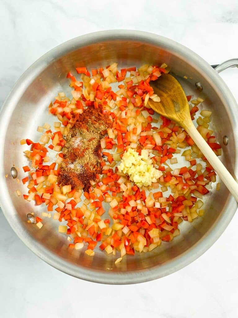 Garlic and spices added to sauteed onion and bell pepper in a stainless steel skill.