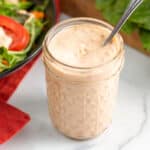 Jar of thousand island dressing with spoon in next to bowl of salad.