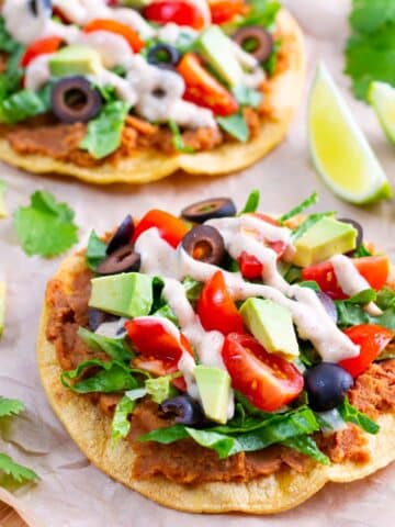Two vegan tostadas with lime wedges and sliced avocado next to them.