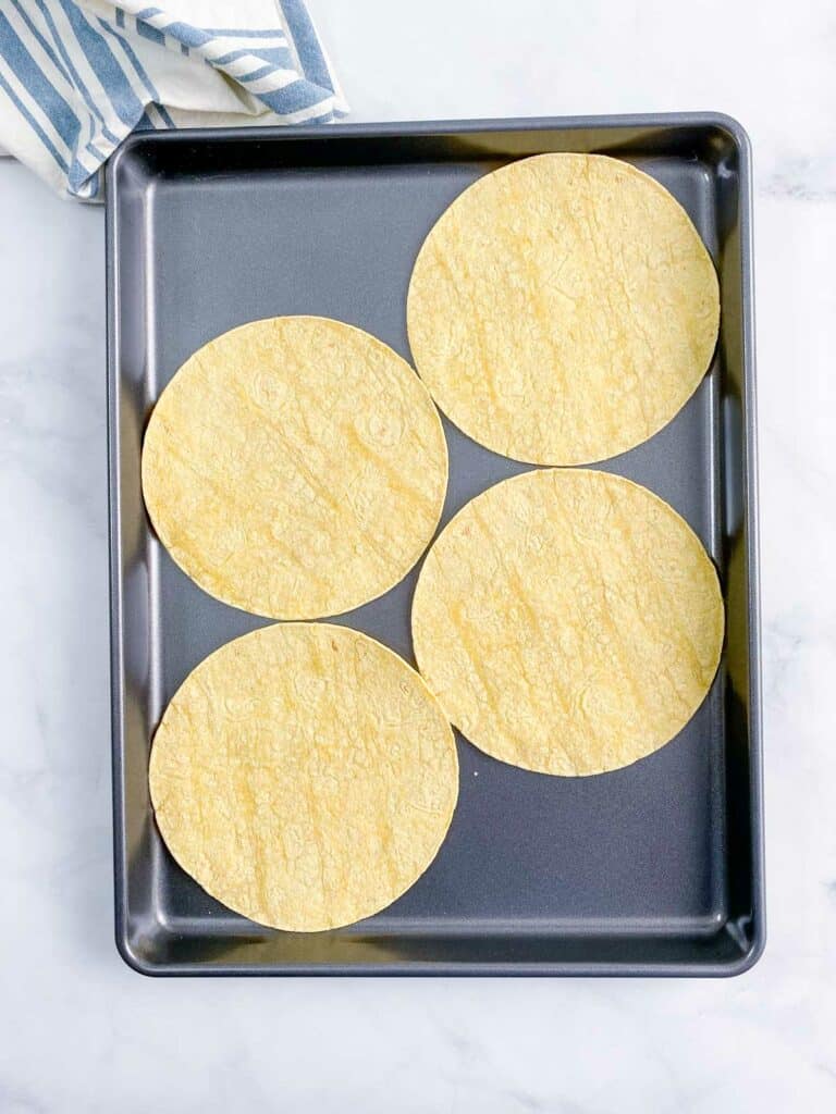 Four corn tortillas on a baking sheet.