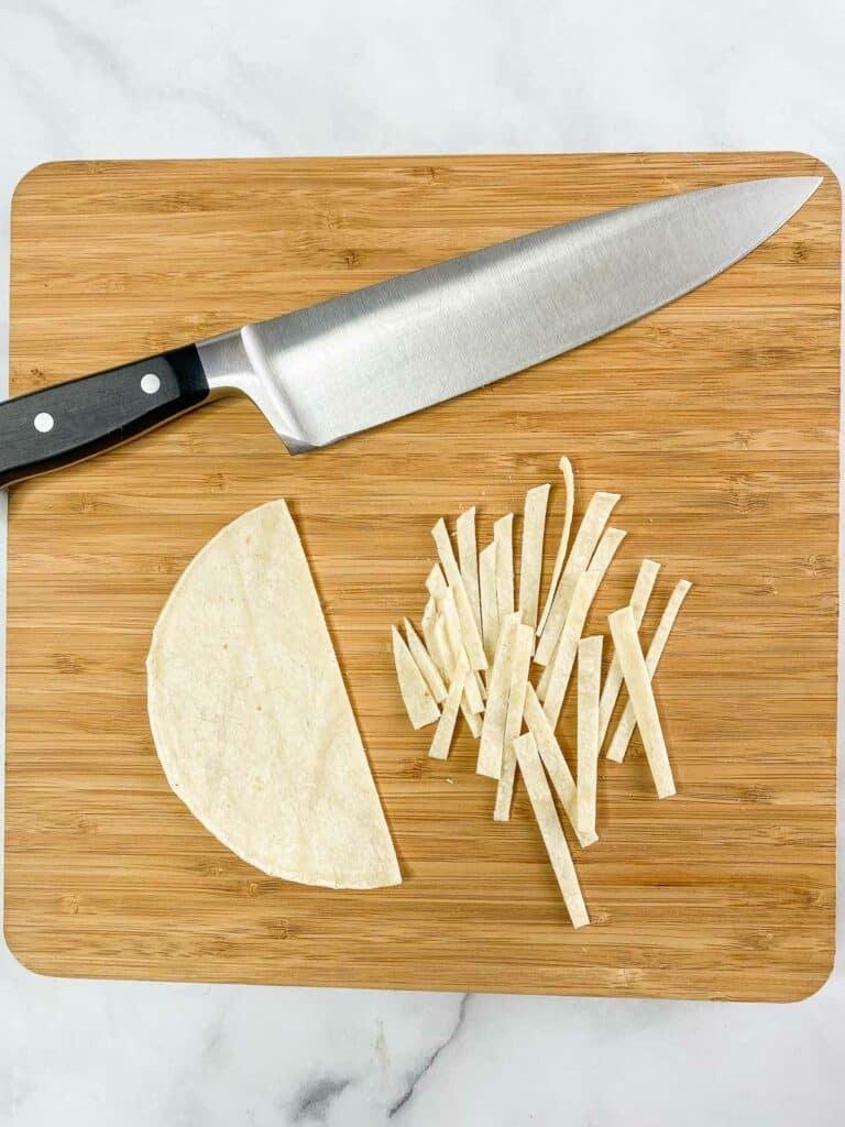 Tortilla being cut into strips on a wooden cutting board.