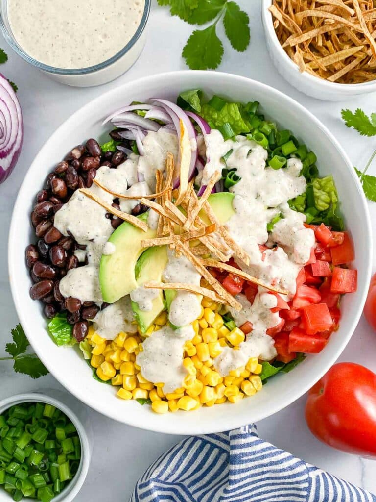 Overhead shot of southwest salad with dressing drizzled on top surrounded by salad ingredients.