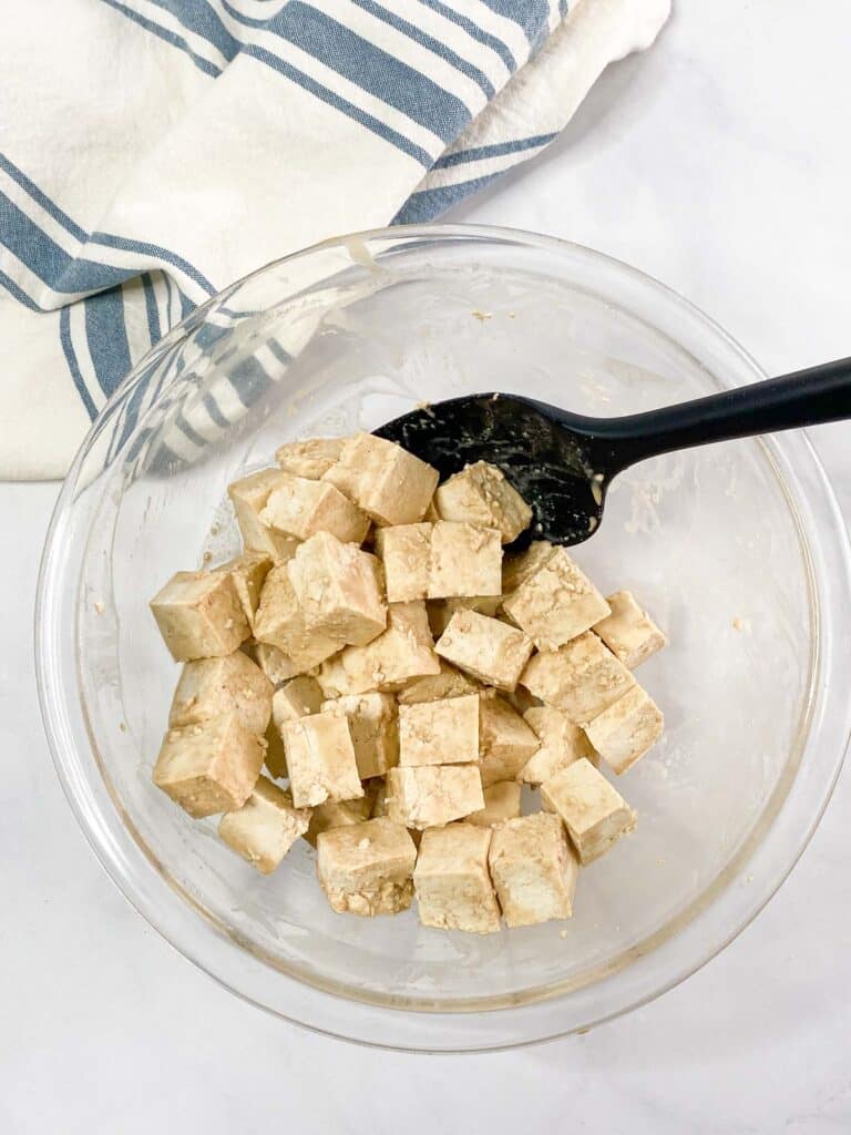 Tofu cubes coated with cornstarch and soy sauce in a glass bowl.