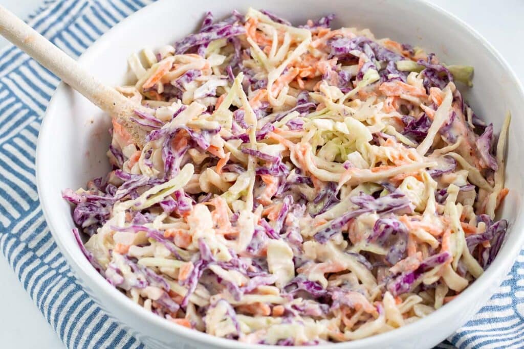 Vegan coleslaw in a white bowl sitting on a blue and white napkin.