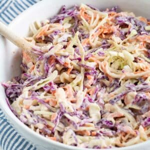 Bowl of coleslaw in a white bowl with a wooden spoon.