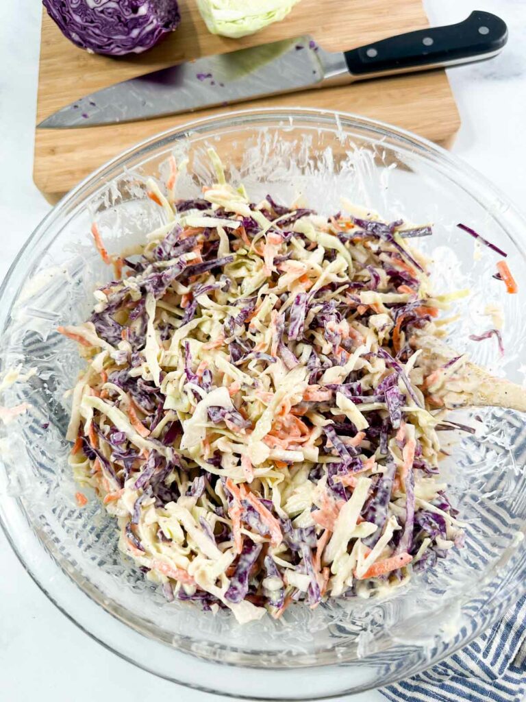 Dressing mixed into shredded cabbage and carrots in a glass mixing bowl.