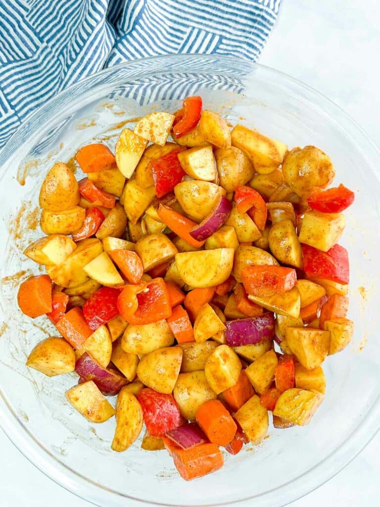 Seasoned potatoes, carrots, onion, and bell pepper in a glass bowl.