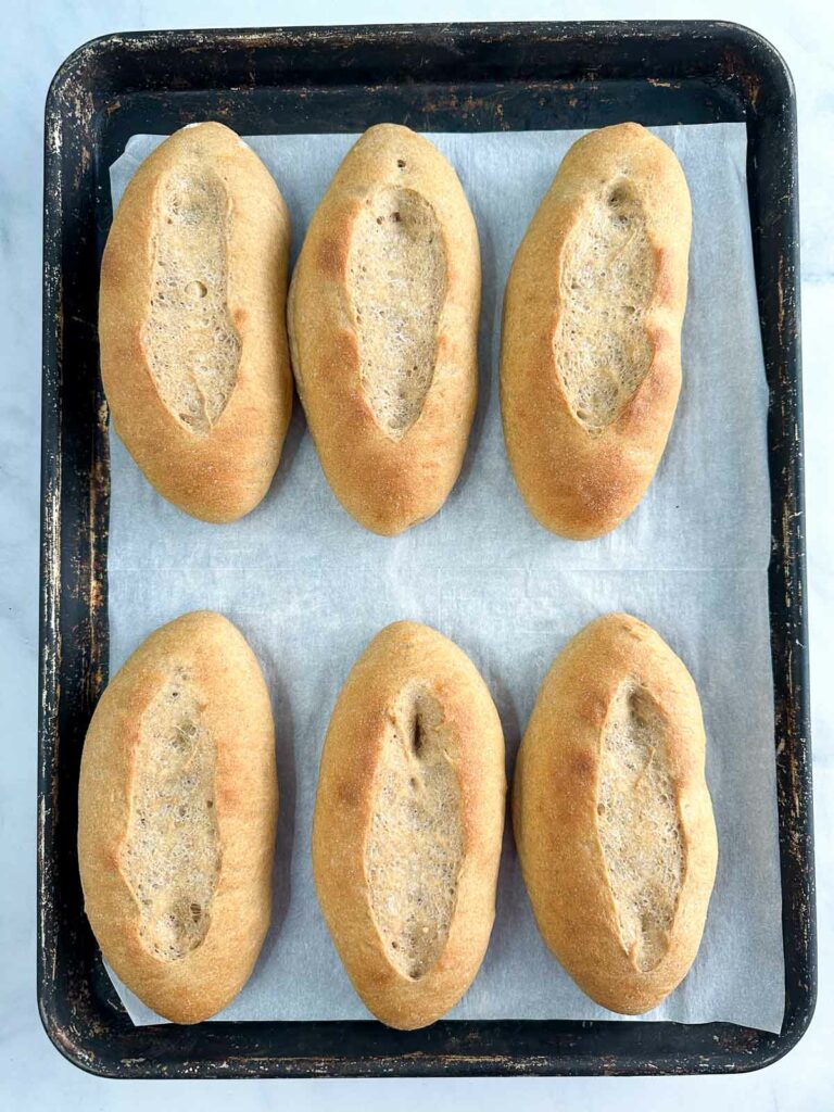 Baked hoagie rolls on a parchment lined baking sheet.