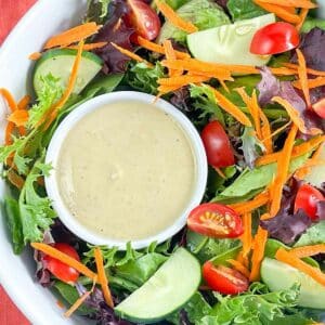Cup of hummus dressing in a large bowl of garden salad.