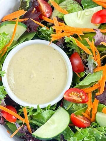 Cup of hummus dressing in a large bowl of garden salad.