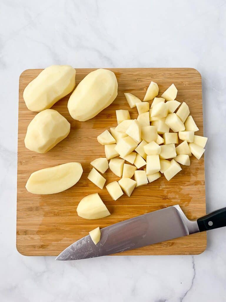 Whole and diced potatoes on a wooden cutting board with a knife sitting next to them.