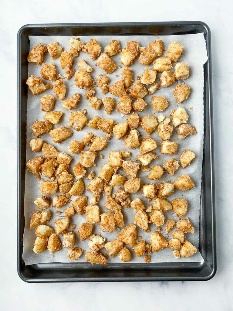Unbaked seasoned diced potatoes on a parchment lined baking sheet.