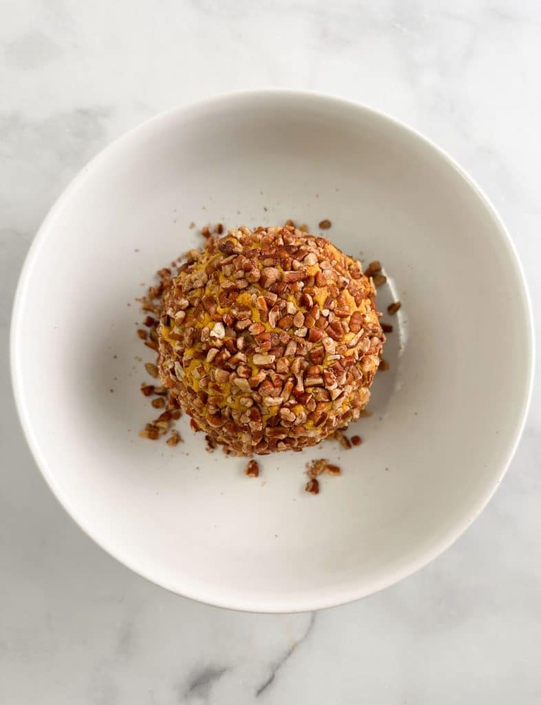 Cheese ball coated with chopped pecans in a white bowl.