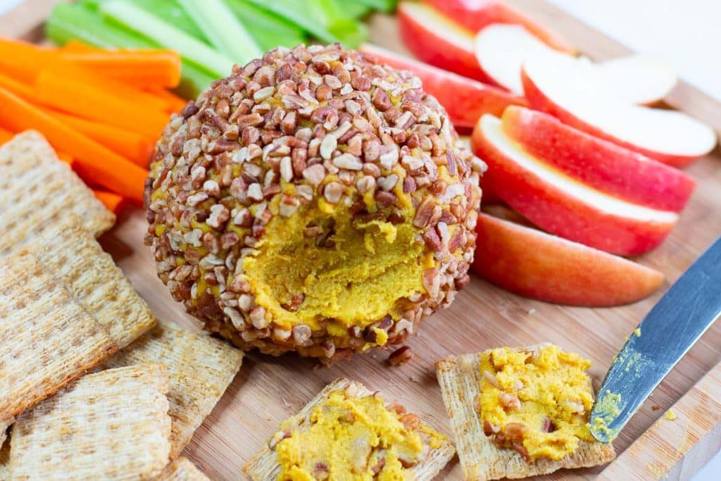 Closeup of cheese ball, crackers, veggies, and apple slices, with cheese ball spread on two crackers.