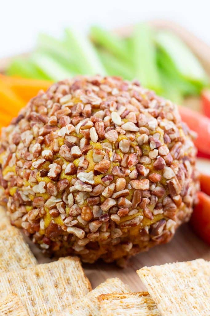 Closeup shot of vegan cheese ball on a board with cracker and veggies.