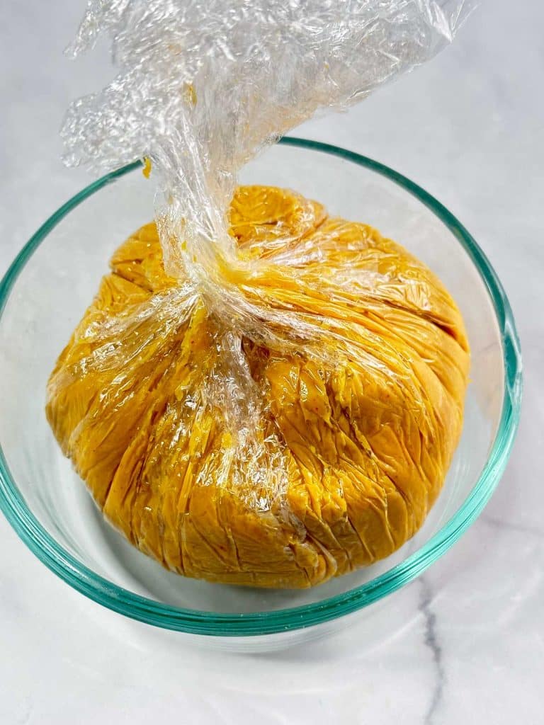 Cheese ball wrapped in plastic wrap sitting in a glass bowl.