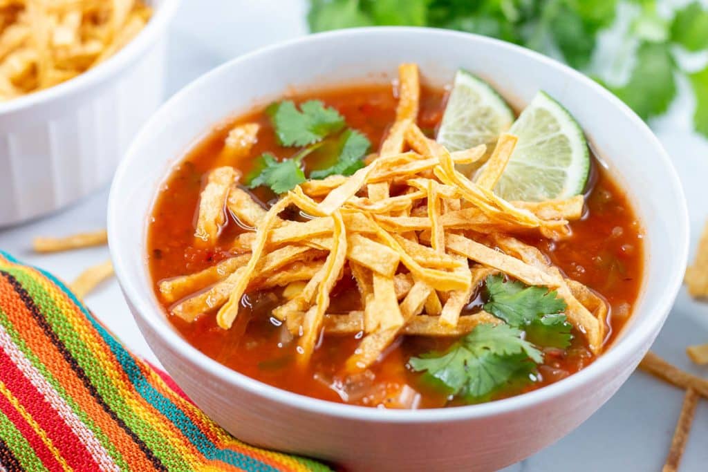 Closeup shot of vegan tortilla soup garnished with tortilla strips, lime slices, and cilantro.