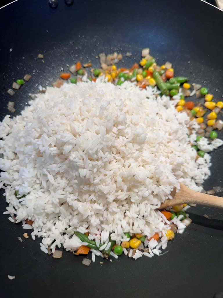 Rice added to the stir fried vegetables in a nonstick wok.