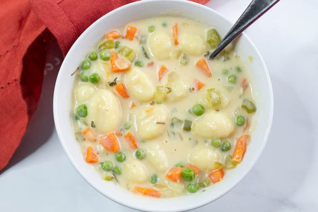 Overhead shot of a bowl of creamy vegan gnocchi soup next to an orange napkin.