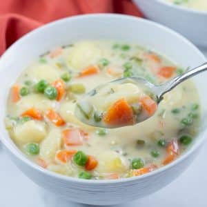 Closeup shot of a bowl of vegan gnocchi soup with a spoonful of soup held above it.