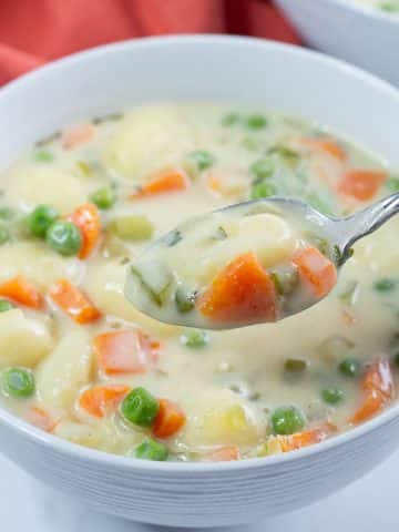Closeup shot of a bowl of vegan gnocchi soup with a spoonful of soup held above it.