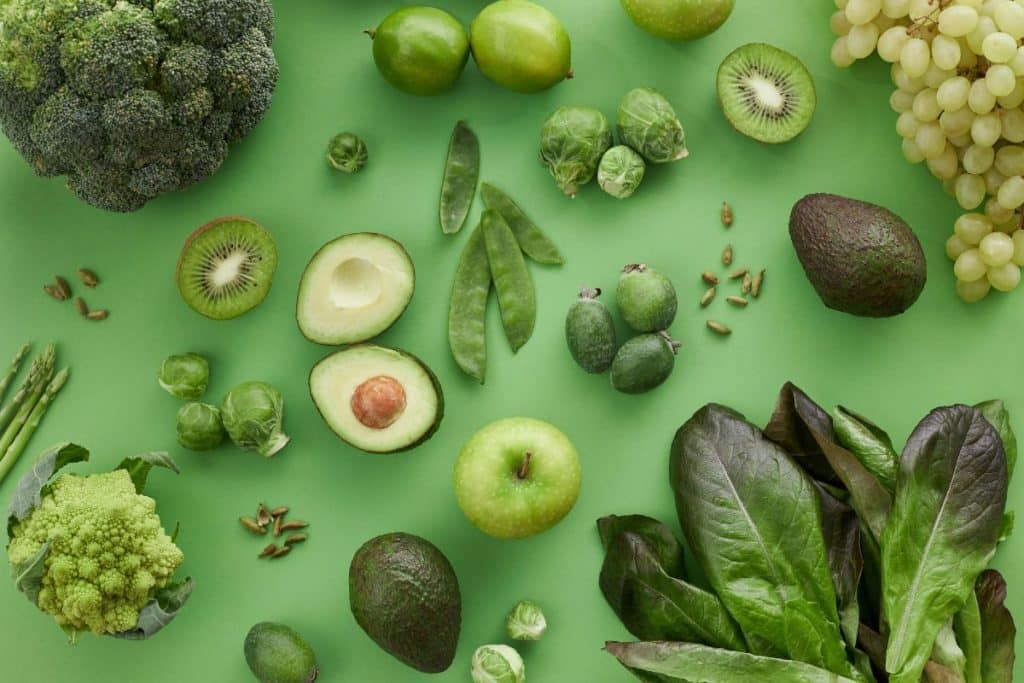 Variety of green fruits and vegetables on a green background.