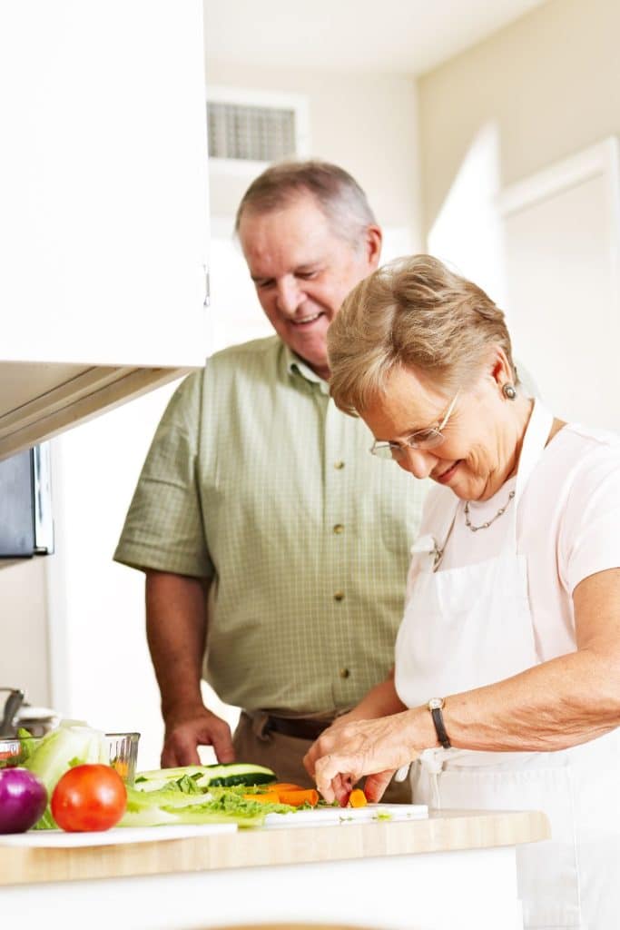 Older couple cooking preparing vegetables together in their kitchen.