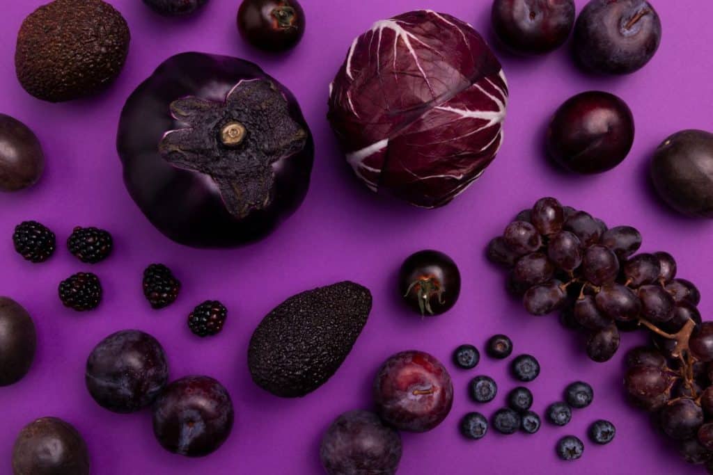 Variety of purple fruits and vegetables on a purple background.