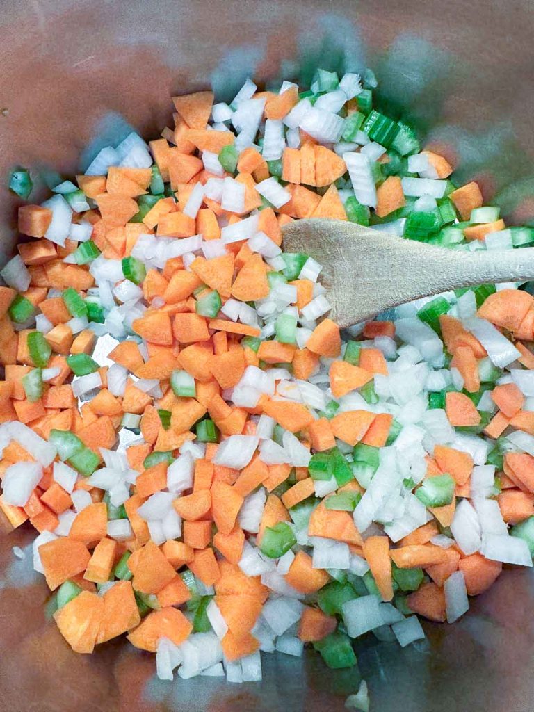 Diced onions, carrots, and celery in a stainless steel pot.